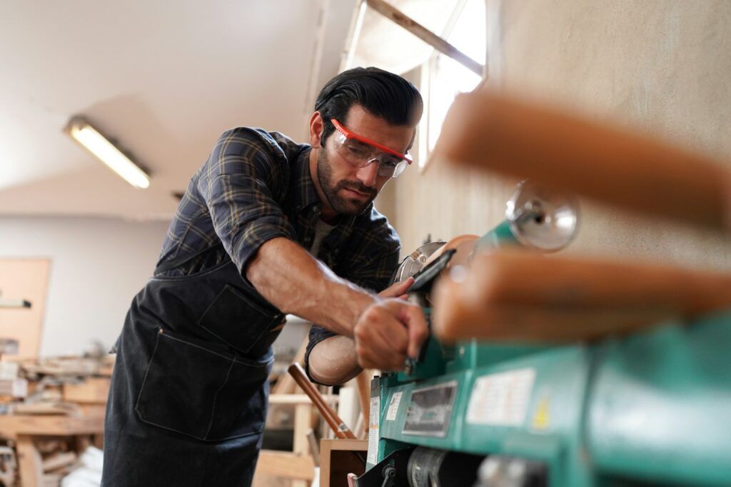 A man is working on a wood lathe in a workshop.