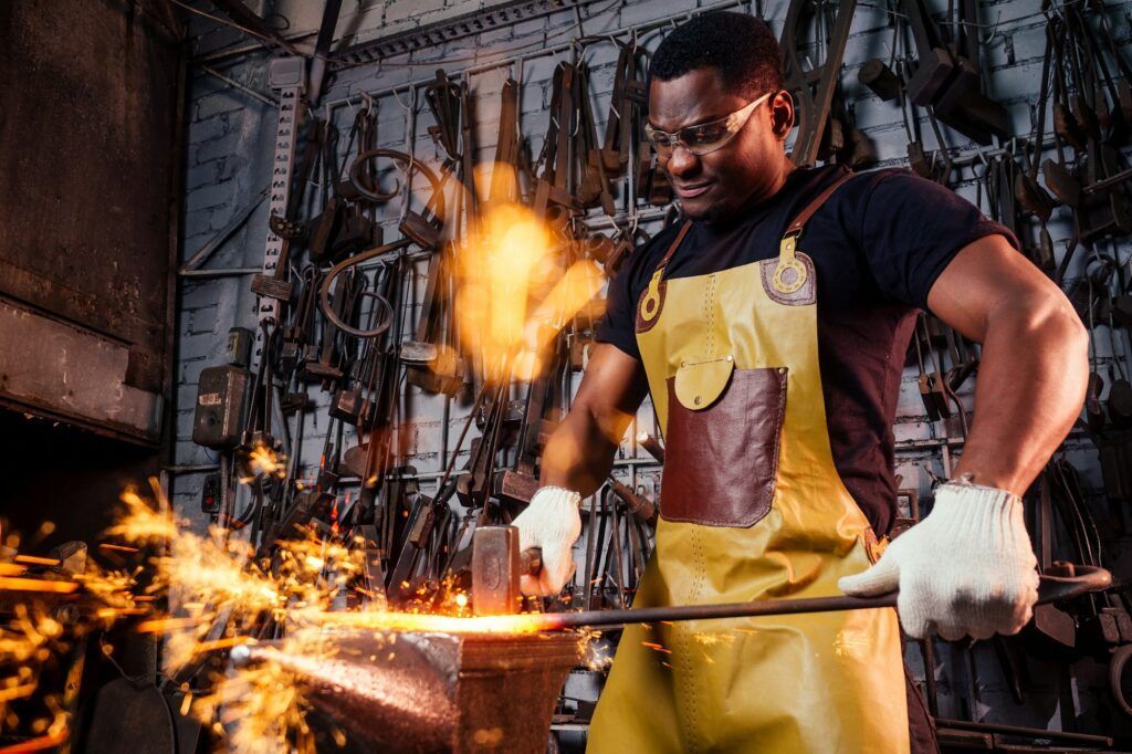 A blacksmith is working on a piece of metal on an anvil in a workshop.