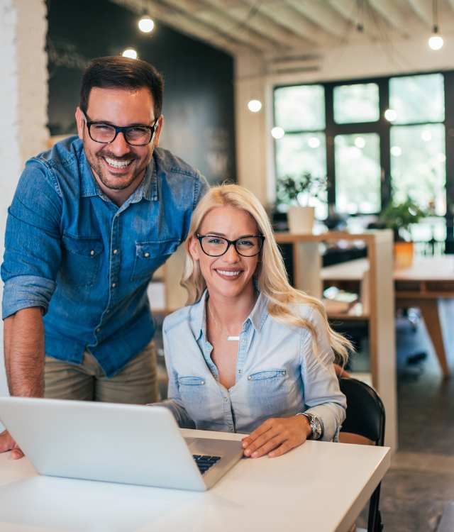 A man and a woman are standing next to each other in front of a laptop computer.