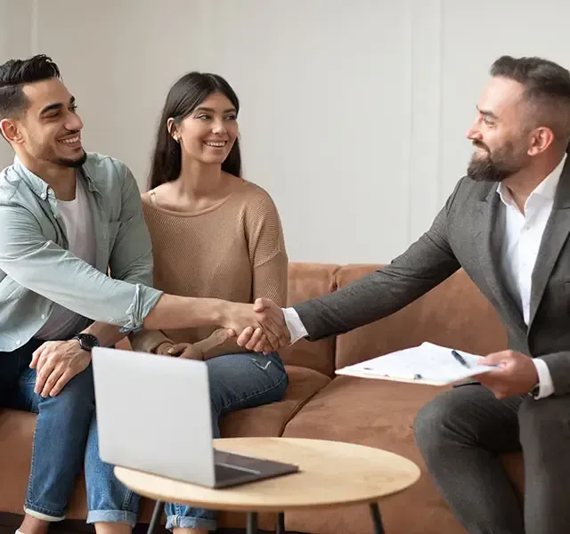 A man and a woman are shaking hands with a man in a suit while sitting on a couch.