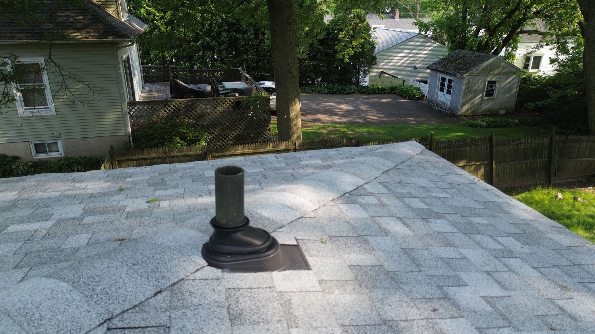 A roof with a chimney on it and a house in the background.