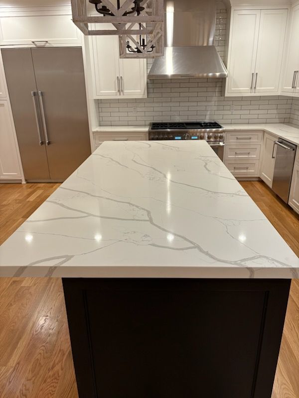 Modern kitchen with white countertops and cabinets, a dark island, stainless steel appliances, and hardwood floors.