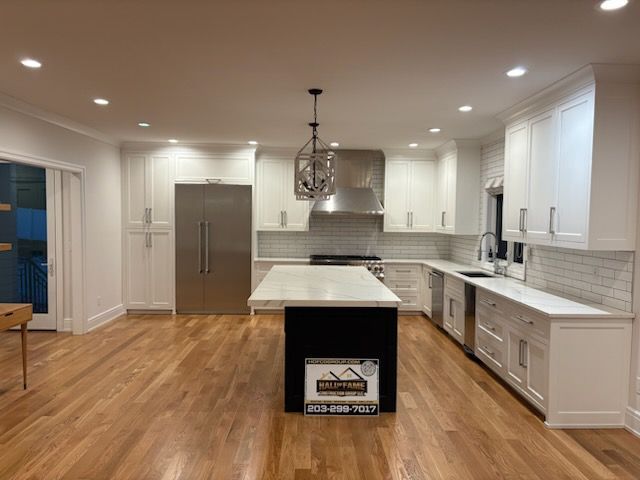 Modern white kitchen with island, stainless steel appliances, and hardwood floors.