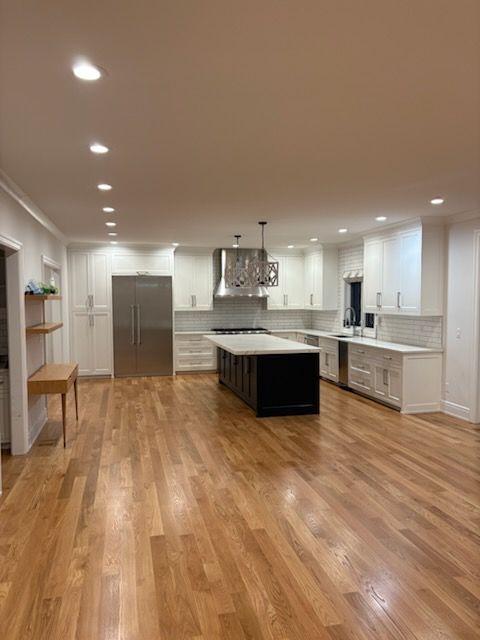 Spacious modern kitchen with white cabinetry, stainless steel appliances, dark island, and wood floors.