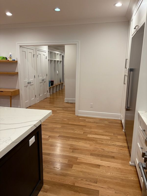 Kitchen with hardwood floors, white walls, dark island, and a view into a hallway with lockers.