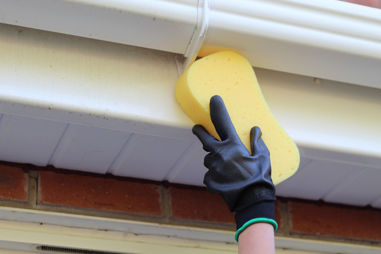 A person is cleaning a gutter with a yellow sponge.