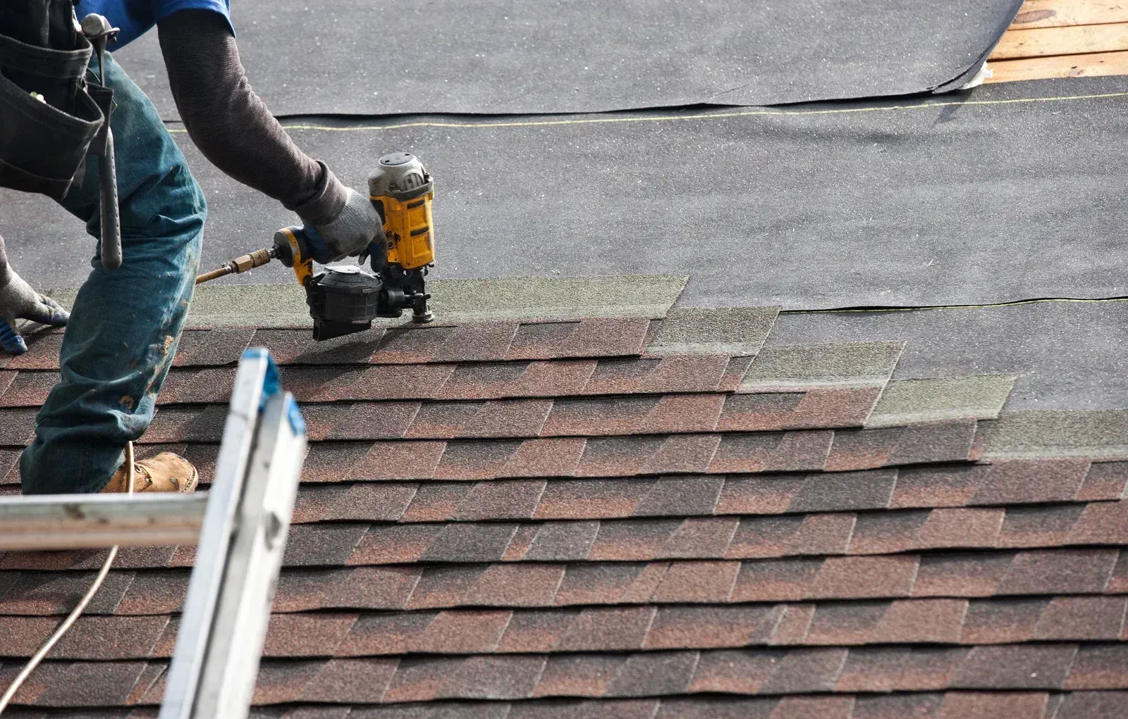 Roofer using a nail gun to install asphalt shingles on a roof.