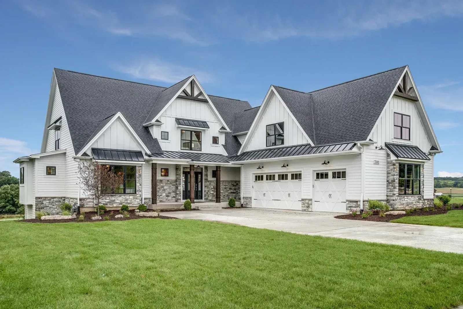 A large white house with a black roof is sitting on top of a lush green field.