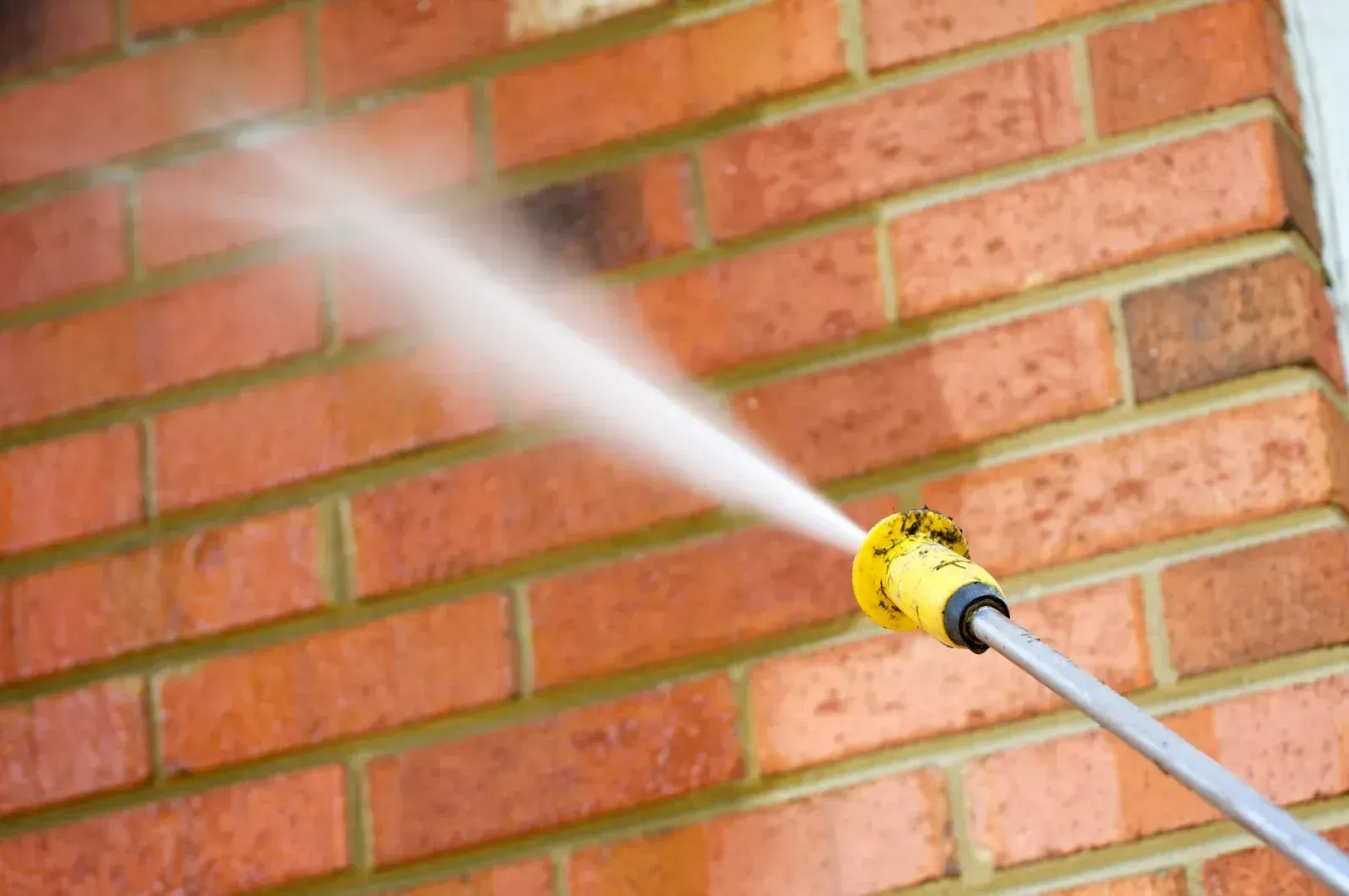 A person is using a high pressure washer to clean a brick wall.