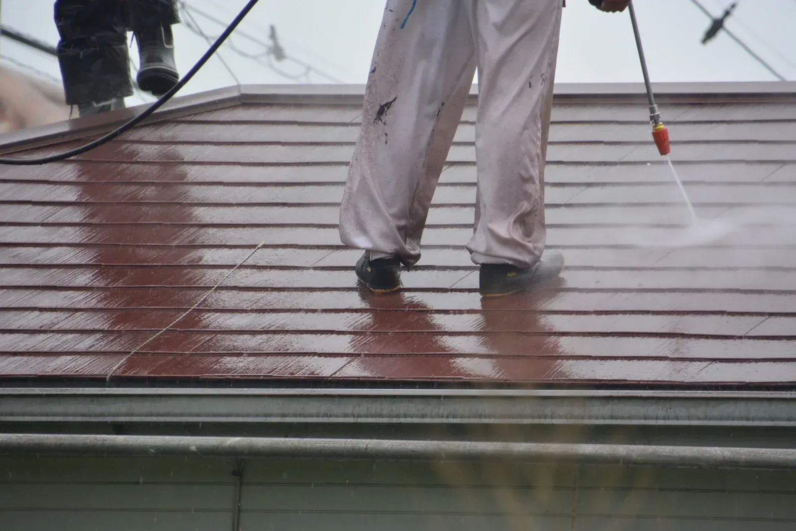 A man is cleaning the roof of a house with a high pressure washer.