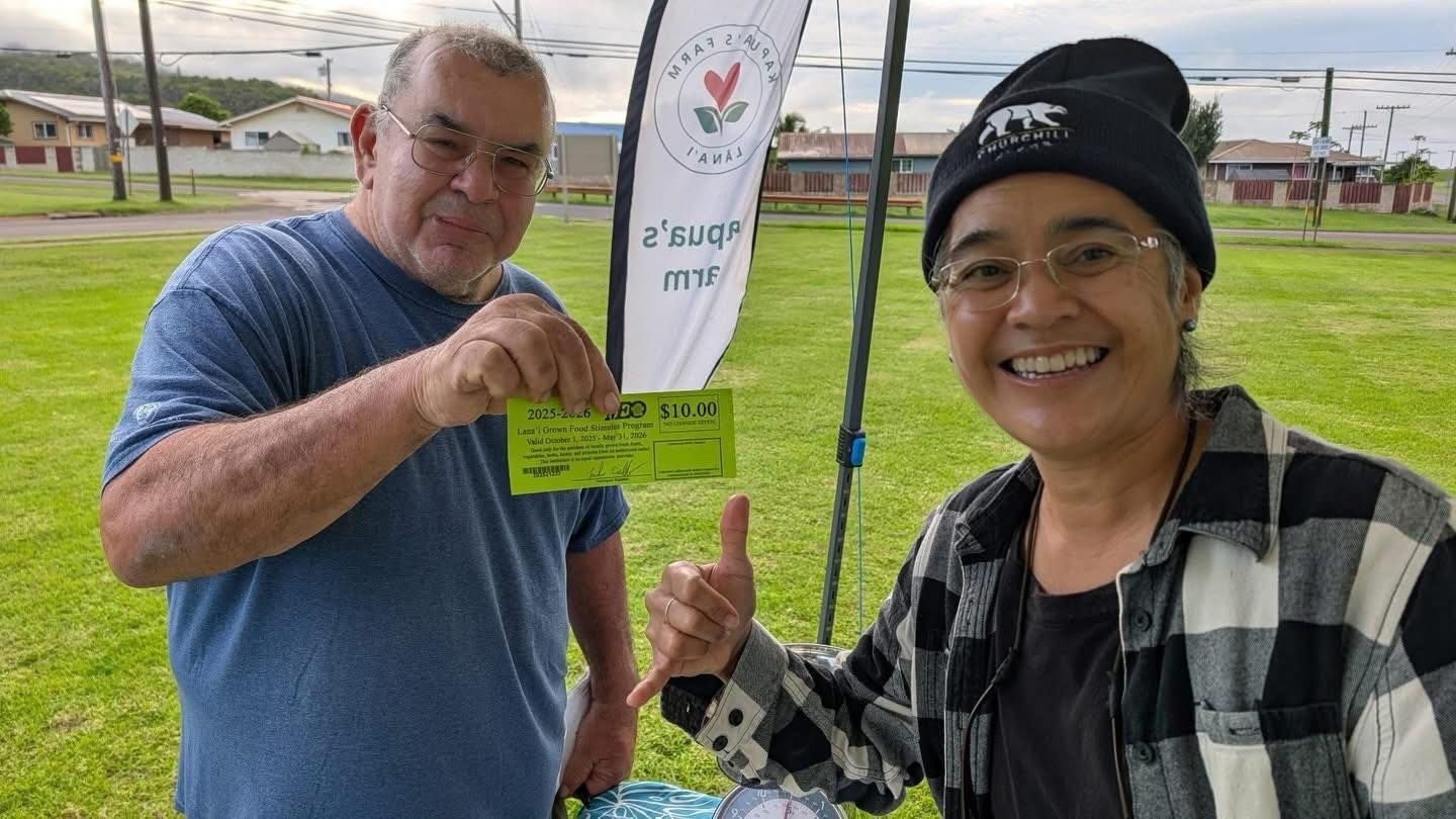 Two people smiling outdoors, holding a sign on a grassy field.