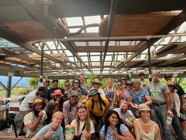 Group of smiling travelers posing under a rustic roof with mountains in the background