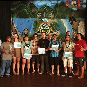Group posing with certificates in front of a colorful HPU mural and beach-themed backdrop