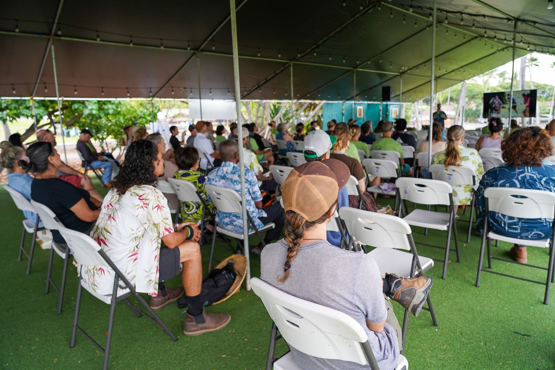 People seated under a large tent at an outdoor gathering on green turf