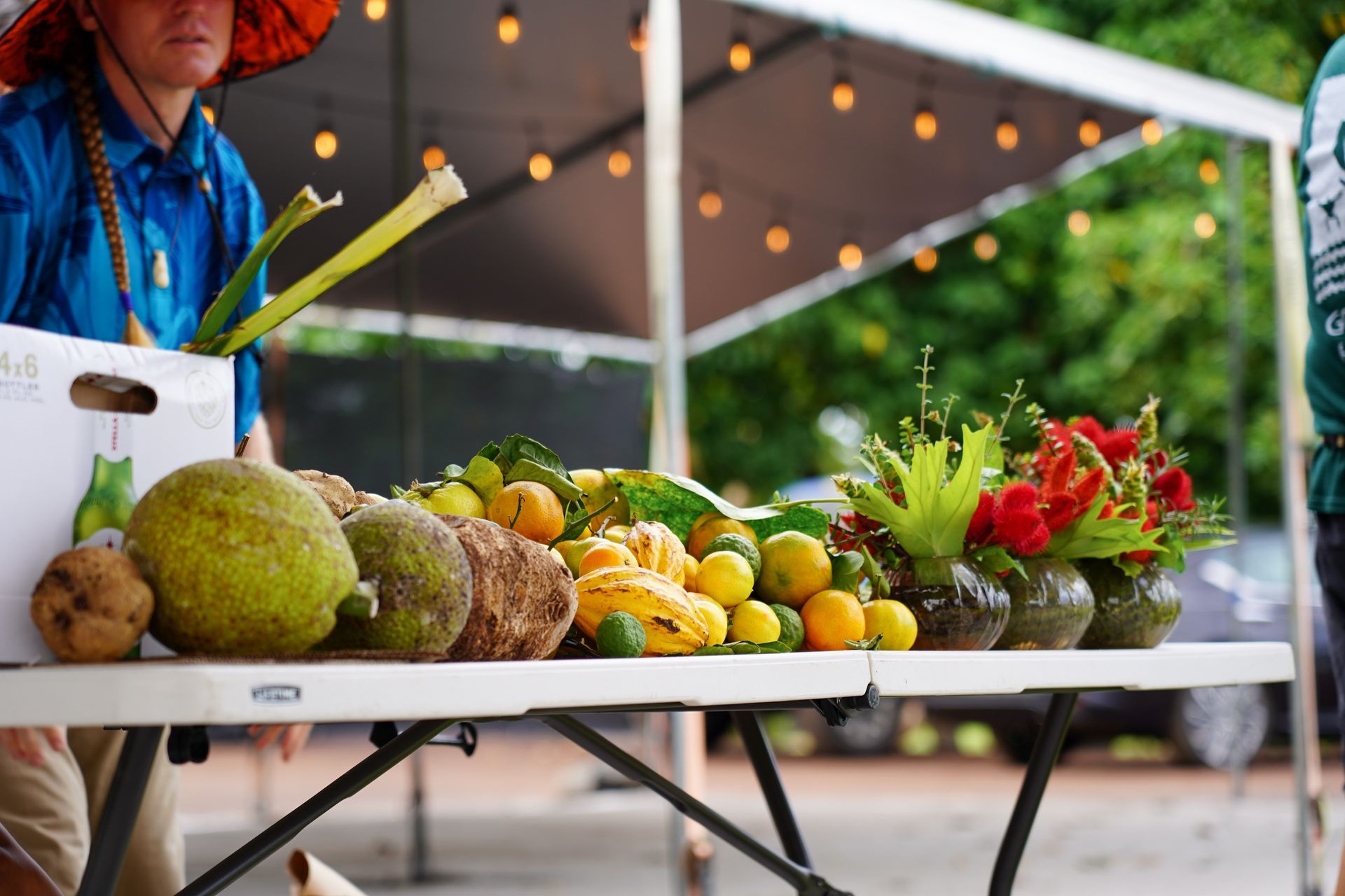 Fresh produce displayed at an outdoor market stall with fruits, vegetables, and flowers in crates