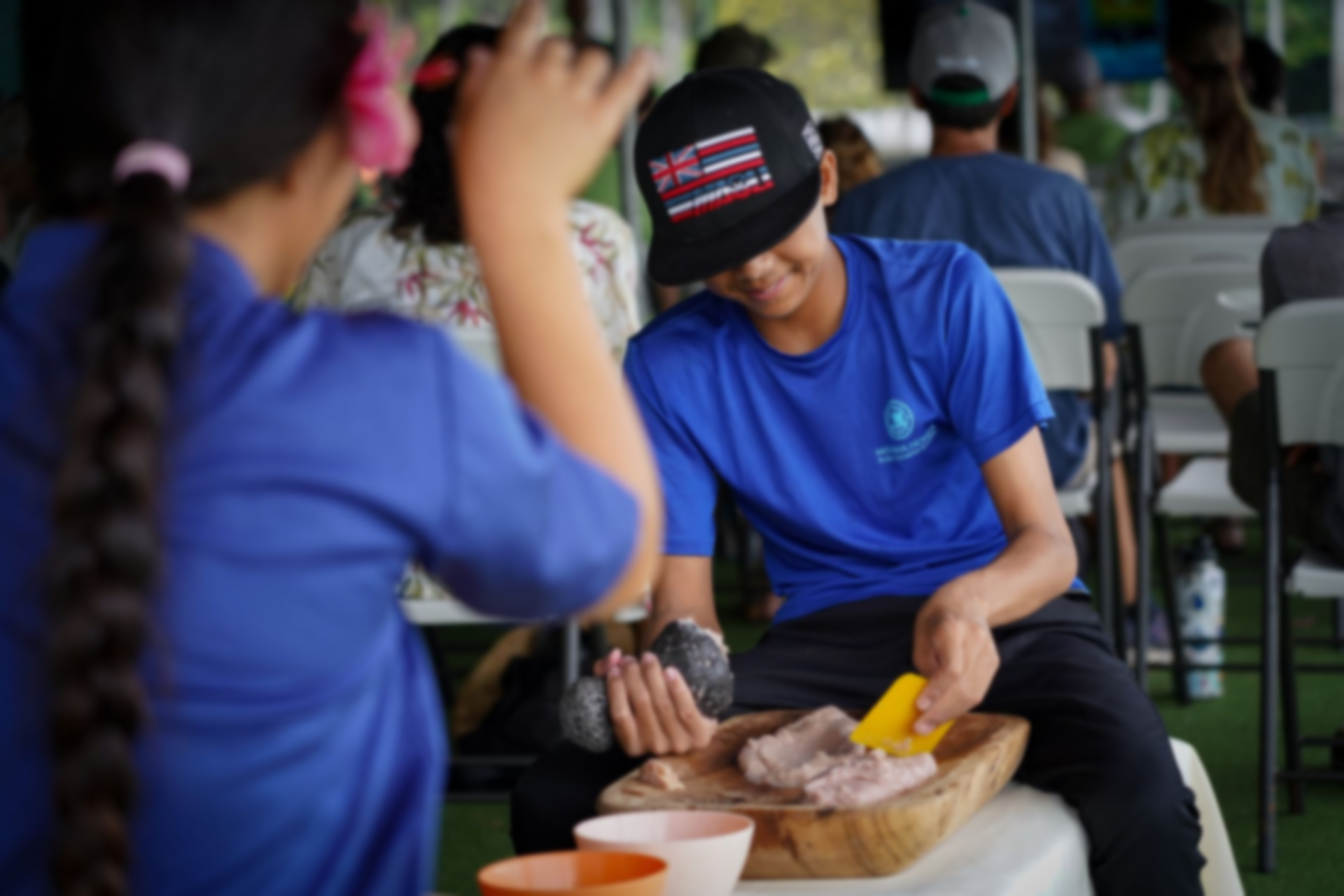 People in blue shirts preparing food at a table in a busy indoor setting