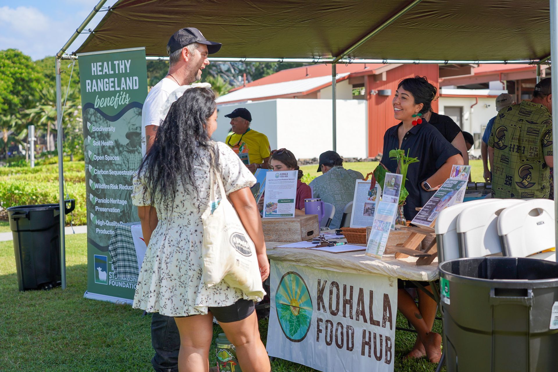 Outdoor market stall with people browsing Korala Food Hub produce under a green canopy.