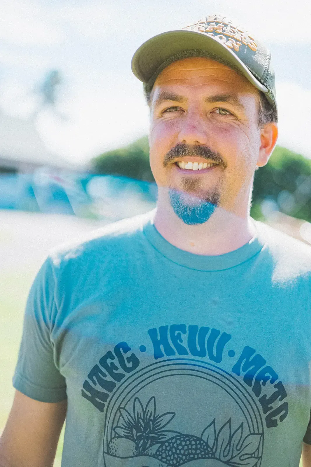 Man in a cap and blue T-shirt smiling outdoors in bright sunlight