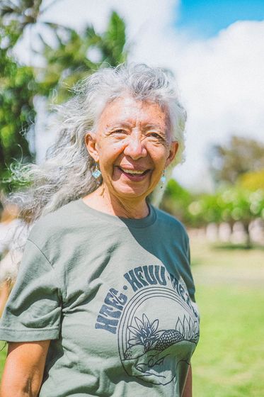 Smiling person with gray hair in a green T-shirt standing outdoors on a sunny lawn