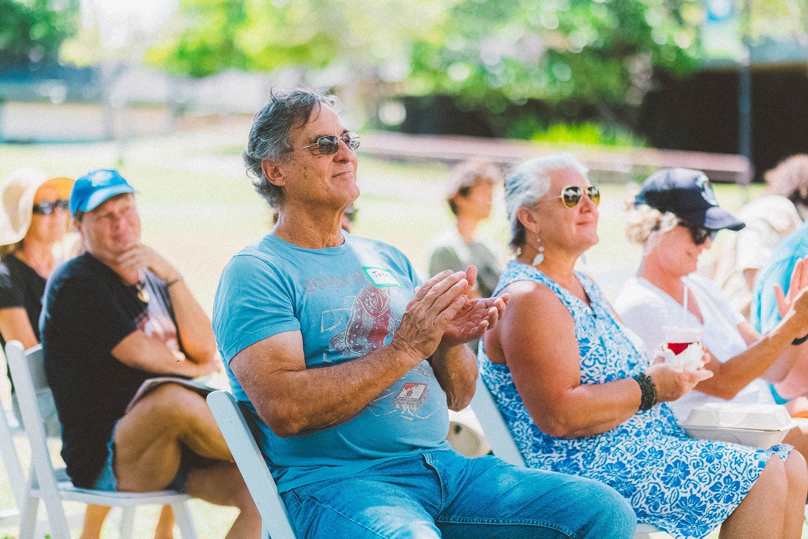 People seated outdoors, clapping at a community event in a sunny park