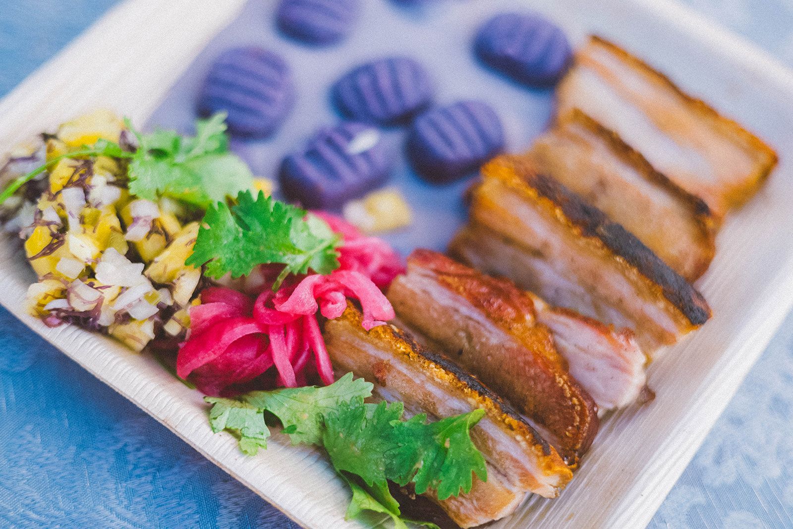 Plated sliced roasted meat with purple potatoes, pickled vegetables, and cilantro on a white dish