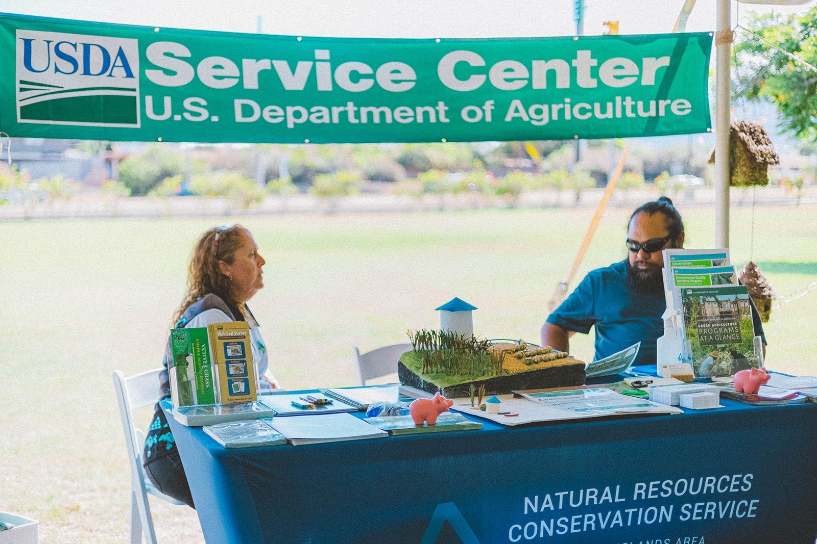 USDA Service Center booth with two people seated behind a display table outdoors