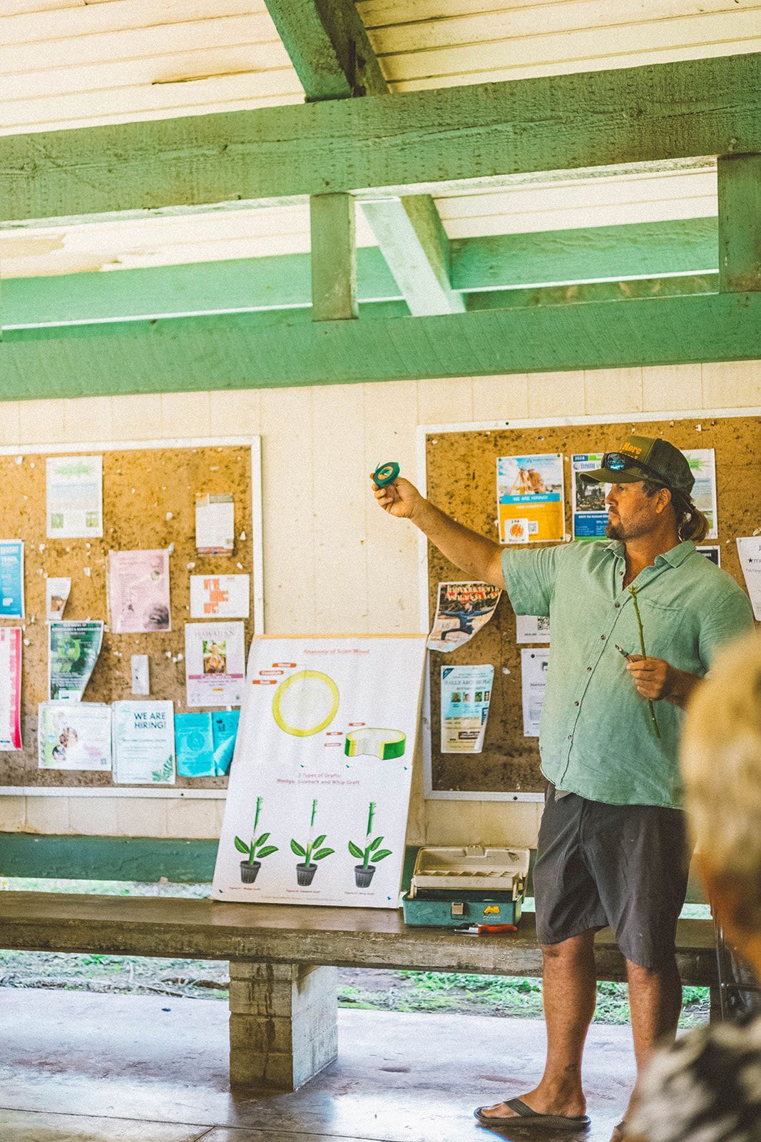 Person presenting a chart on a bulletin board inside a rustic, open-air classroom