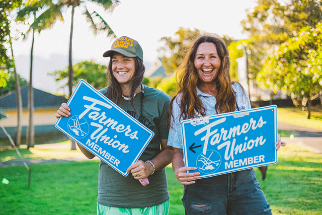 Two people smiling and holding Farmers Union Member signs outdoors on grass
