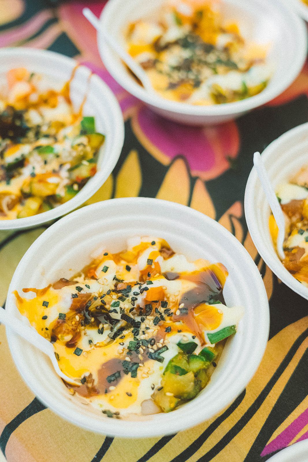 Small cups of colorful noodle or salad dishes topped with herbs on a patterned tablecloth