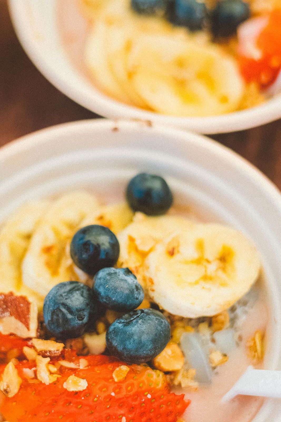 Bowls of oatmeal topped with banana slices, blueberries, and red fruit on a wooden table