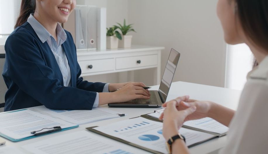 Two Women Are Sitting At A Table With A Laptop — Loretta Davison Financial Solutions In Shellharbour, NSW 