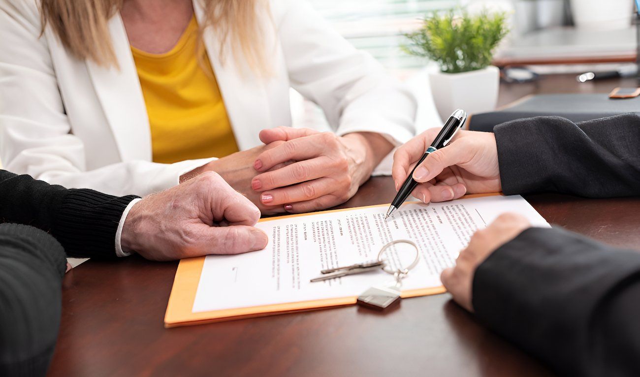 A Group Of People Are Sitting At A Table Signing A Document — Loretta Davison Financial Solutions In Austinmer, NSW 