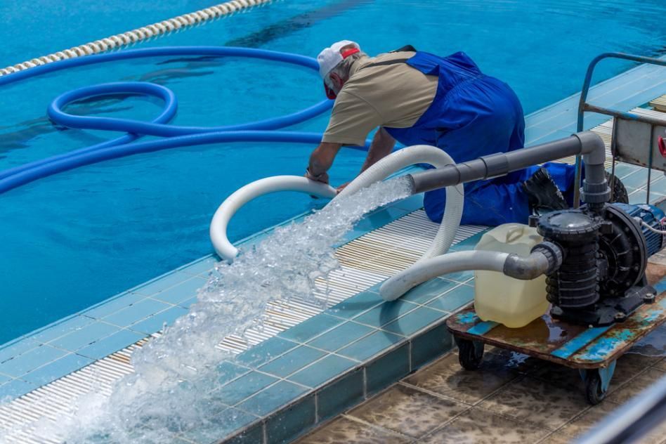 A Man is Cleaning a Swimming Pool With a Hose — Whitsunday Pool Service in Proserpine, QLD