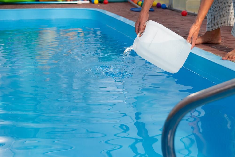 A Person is Pouring Water Into a Swimming Pool — Whitsunday Pool Service in Proserpine, QLD