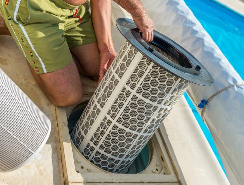 A Man is Kneeling Down to Remove a Filter From a Swimming Pool — Whitsunday Pool Service in Airlie Beach, QLD