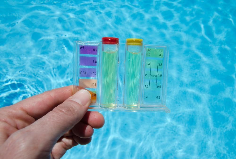 A Person is Holding a Test Tube in Front of a Swimming Pool — Whitsunday Pool Service in Airlie Beach, QLD