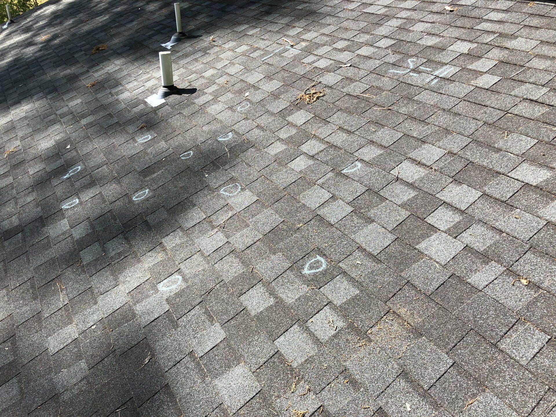 Image of old asphalt shingle roof with hail damage marked by chalk. 