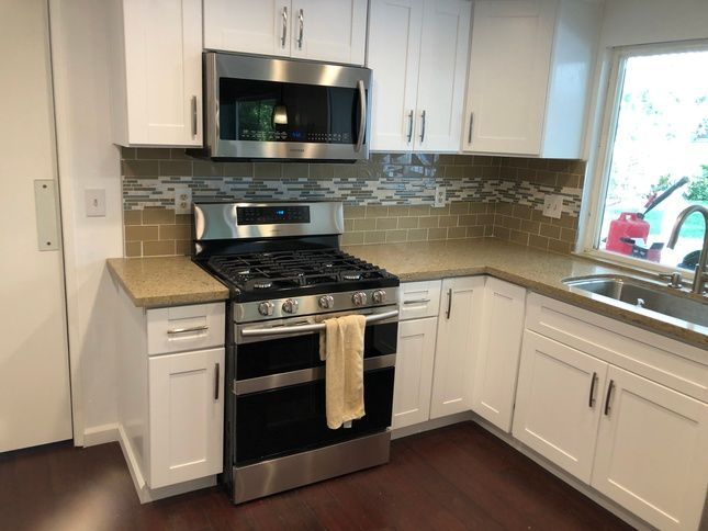 White kitchen with stainless steel appliances, backsplash, and cabinets, next to a window.