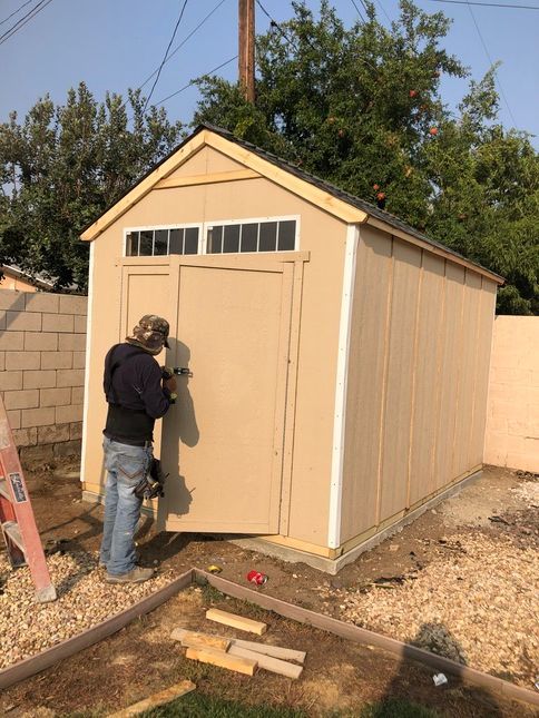 Person installing a door on a tan shed in a yard.