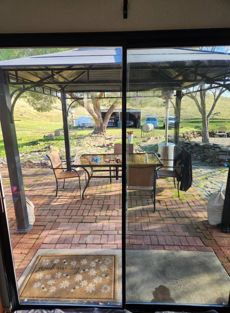 Sliding glass doors opening to a brick patio with a pergola, table, chairs, and a grassy yard beyond