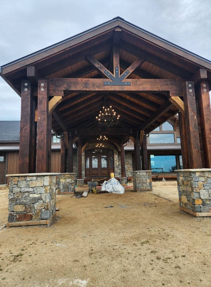 Rustic covered entrance with wood beams, stone pillars, and a chandelier over a gravel path