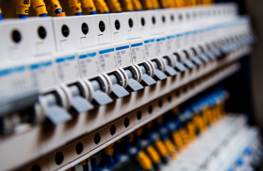 Close-up of rows of electrical circuit breakers in a panel, with white and gray switches against a blue background