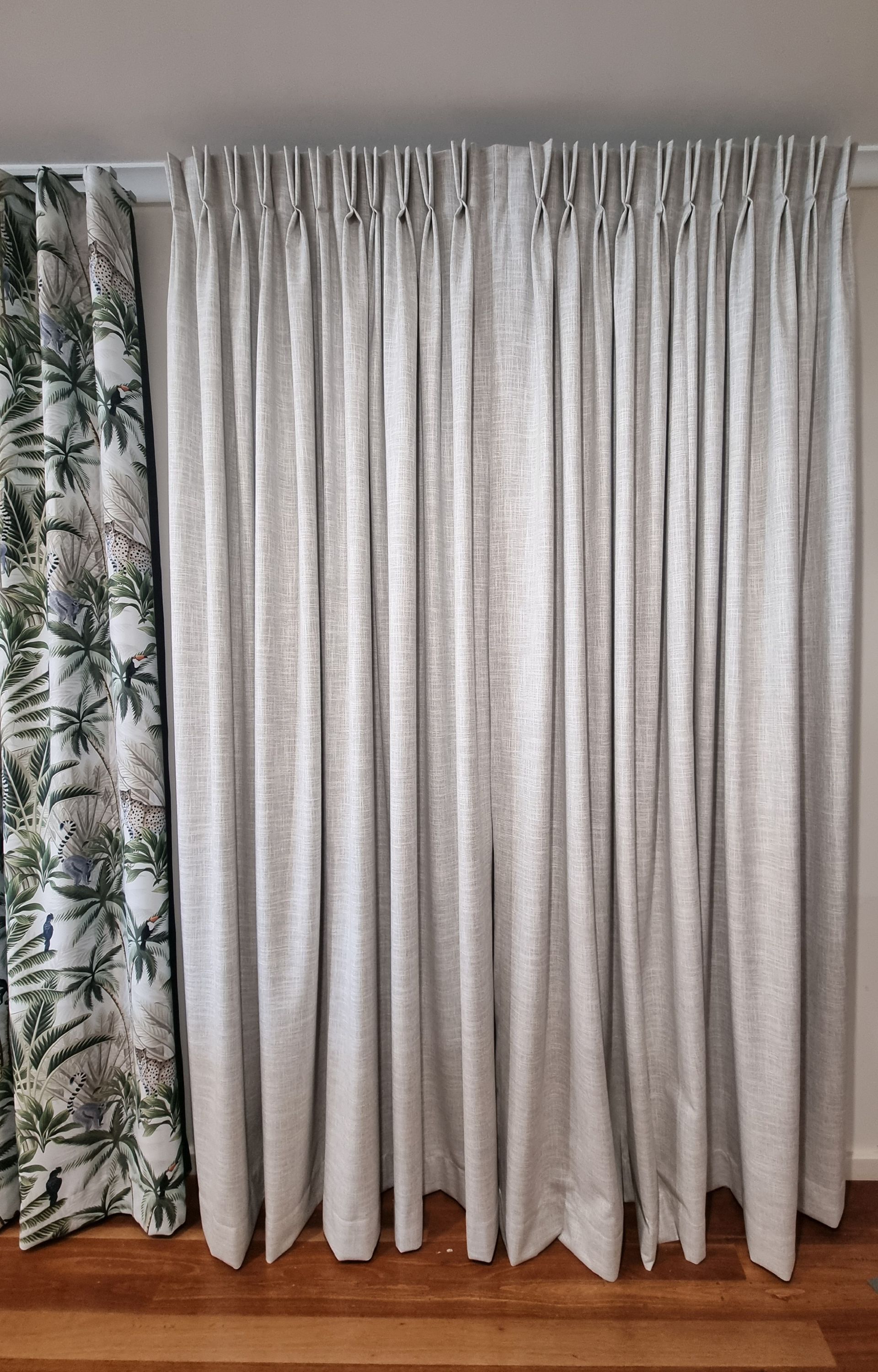 A bedroom with grey curtains in the middle and patterned curtains to the left — Winning Blinds in Cardiff, NSW