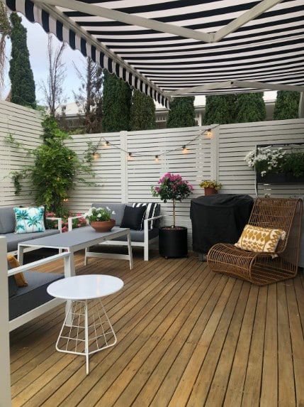 Outdoor Patio With Striped Awning, White Furniture, And Wooden Deck — Winning Blinds in Cardiff, NSW
