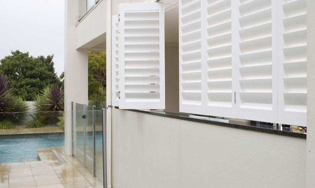 A white house with a swimming pool in the background and shutters on the windows — Winning Blinds in Cardiff, NSW