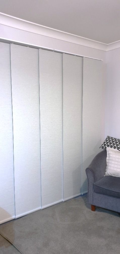 A dining room table with white blinds to the left and a couch with patterned pillows on it to the right— Winning Blinds in Cardiff, NSW