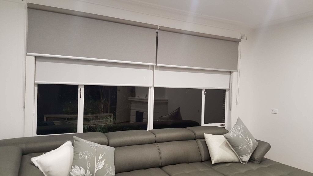 roller blinds in front of a grey leather couch that are white  — Winning Blinds in Cardiff, NSW