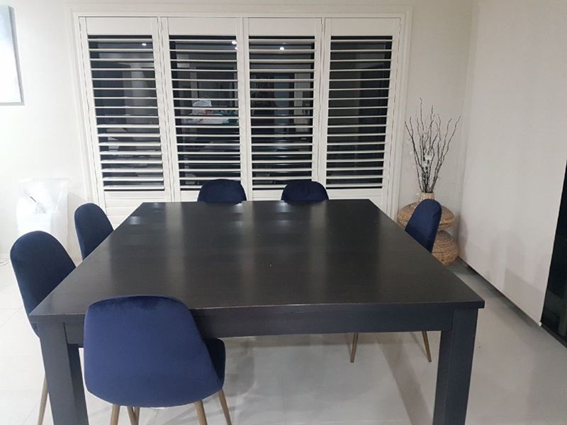 Room With A Table And Chairs In Front Of Shuttered Windows — Winning Blinds in Cardiff, NSW
