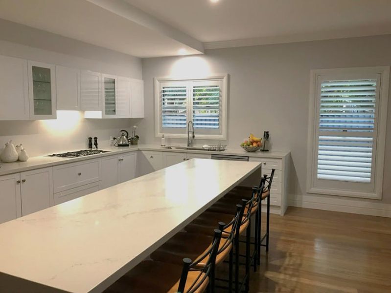 White Kitchen With Island, Stools, And Window Shutters — Winning Blinds in Cardiff, NSW