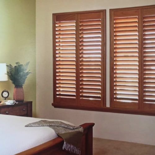 A Bedroom With a Bed and Two Windows With Wooden Shutters — Winning Blinds in Cardiff, NSW